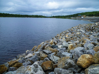 Fototapeta premium The shore of the lake, neatly stacked with large stones on a summer day.