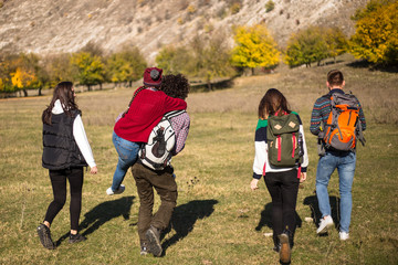 Five friends capturing from the back how going to their exhibition in the mountain, walking tired but with a good mood, they have big trip bags