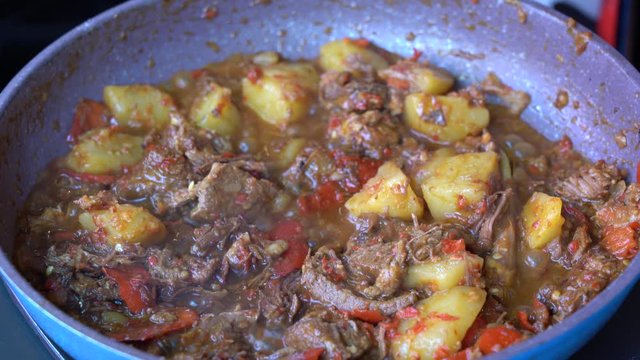 Frying pan with onion, lemongrass, red pepper and beef meat, close up. Indonesia. Sambal Goreng Ati Kentang, Indonesian cuisine, spicy beef meet and potatoes garnish with lemongrass leaf and red chili