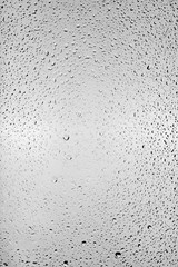 Drops of water flow down the surface of the clear glass on a gray background.