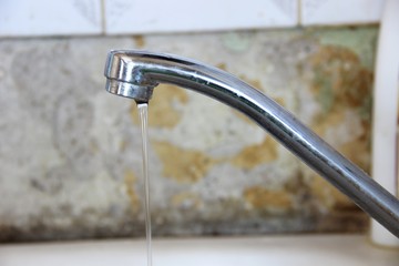 a thin stream of water flows from the tap, close-up. silver colored kitchen faucet on old wall...