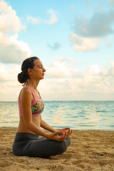 Yoga lifestyle. Young woman meditating, practicing yoga and pranayama with gyan mudra at the beach,...