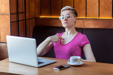 Portrait of confident egoist young girl with short hair in pink t-shirt and eyeglasses is sitting...