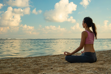 Fototapeta na wymiar Yoga lifestyle. Young woman meditating, practicing yoga and pranayama with gyan mudra at the beach, Bali