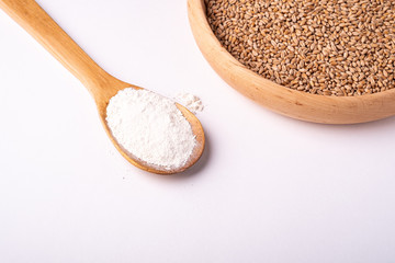 Wheat seeds grains in wooden bowl near with flour in spoon spatula, angle view, isolated on white background, copy space
