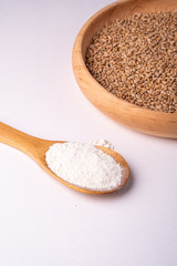 Wheat seeds grains in wooden bowl near with flour in spoon spatula, angle view, isolated on white background, copy space