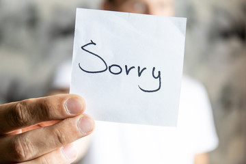 man holds in his outstretched hand a sheet with the inscription "Sorry"