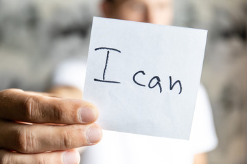 man holds in his outstretched hand a sheet with the inscription "I can"