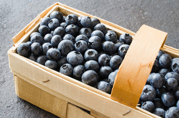 Fresh organic blueberries in basket on dark concrete background.