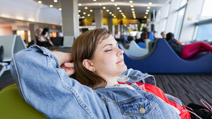 Tired female traveler sleeping on the airport departure gates bench with a suitcase sleep on a chair at the airport and waiting for her flight. Tiring travel concept.