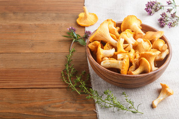 Chanterelle mushrooms in wooden bowl and spice herbs on wooden background with linen textile, side view.