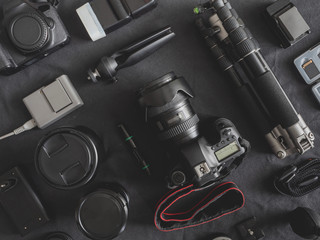 top view of work space photographer with digital camera, flash, cleaning kit, memory card, tripod and camera accessory on black table background