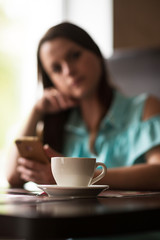 A cup of coffee on a table in a cafe in the background a girl. The girl is out of focus.