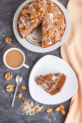 Homemade cake with milk cream, cocoa, almond, hazelnut on a black concrete  background with orange textile and a cup of coffee. Top view, copy space.