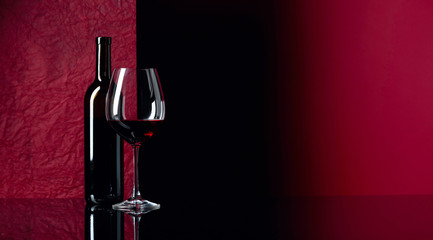 Bottle and glass of red wine on a black table.