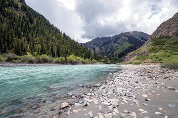mountain river with turquoise water with a bank of gray pebble sand and stones of various sizes...