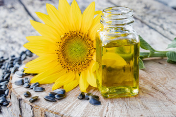 Sunflowers and seeds on a wooden background near sunflower oil in a glass jar. Healthy foods and fats.