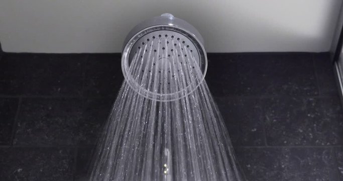 A detail view of a round, upscale shower head fixture as the water turns on then off.  	