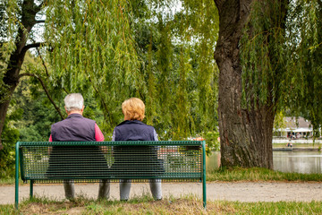 Älteres Paar auf einer Bank im Park an einem See, Aufnahme von hinten,