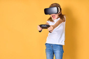 Girl experiencing VR headset vs joystick game on yellow background. Surprised emotions on her face. Child using a gaming gadget for virtual reality. Futuristic goggles at young age. Virtual technology