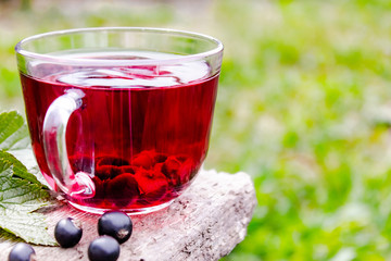 Glass cup of fruit tea with black currant berries on a wooden table in the open air.