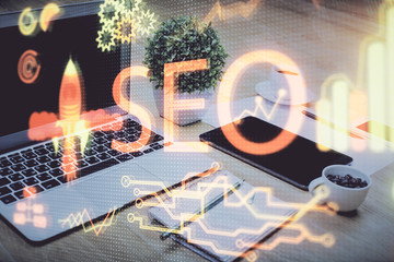 Double exposure of table with computer and seo drawing hologram. Search optimization concept.