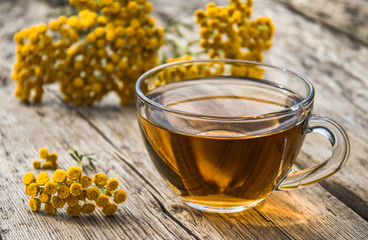 Tansy infusion in a glass cup on a wooden table. Tansy Herbal tea. Healing herbs.