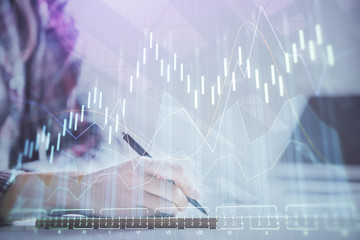 A woman hands writing information about stock market in notepad. Forex chart holograms in front....