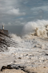 Naklejka na ściany i meble Huge breaking waves next to a lighthouse on a stormy day (Porthcawl, Wales, UK)