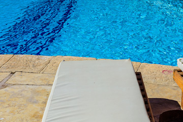 Chaise lounge near the swimming pool with clear water
