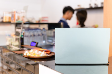 Laptop on counter coffee bar with barista working in bur background.