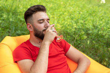 A young man with a beard lies on an Lamzac inflatable sofa and drinks a alcoholic drink from a glass. Enjoying the rest