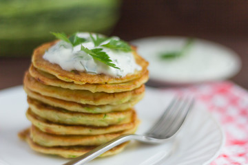 delicious homemade zucchini pancakes with sour cream and herbs on a wooden background