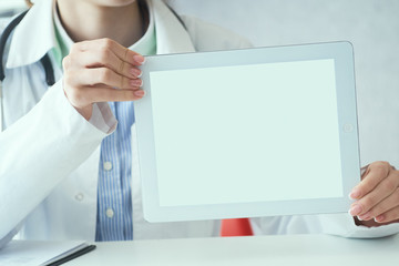 Middle section of female medicine doctor shows tablet computer with white screen. Contact information exchange, introducing gesture at formal meeting concept