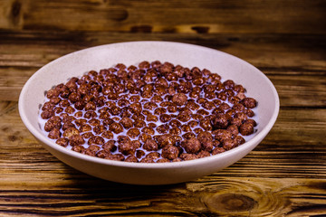 Ceramic plate with chocolate cereal balls in milk on wooden table