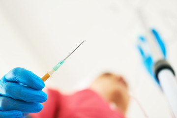 Hand in blue sterile glove holds needle from a plastic dropper system. Nurse is ready to put a dropper to the patient.