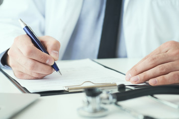 Mid section of male doctor writing write prescription to patient at worktable. Panacea and life save, prescribing treatment.