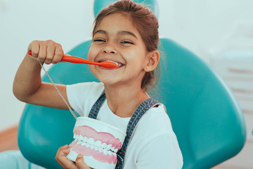 smiling mixed raced girl brushing teeth at dental clinic - obrazy, fototapety, plakaty