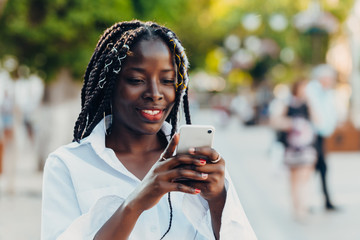 Portrait of a smiling young African American girl with pigtails with a phone walking on the street...