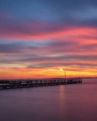 Fototapeta na wymiar Vibrant colors light up the sky just after sunset over a long fishing pier. Jones Beach, Long Island New York