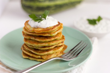 fresh delicious zucchini pancakes with sour cream and herbs on the table