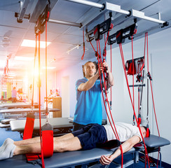 Obraz na płótnie Canvas Physiotherapy. Suspension training therapy. Young man doing fitness traction therapy with suspension-based exercise training system.