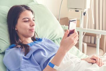 beautiful young patient women lying in  hospital bed and smiling with smart mobile phone while...