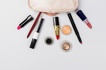 A pink makeup bag with cosmetic beauty products spilling out on to a light  background, with empty space at side