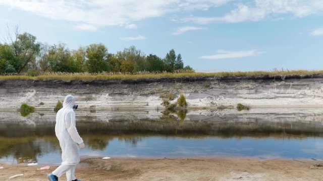 A man in a protective suit and respirator walks along a dry river and estimates the extent of the pollution. Humanity is poisoning the planet Earth. Ecological catastrophy. Anthropogenic influence. 4K
