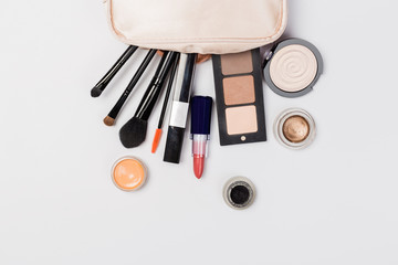 A pink makeup bag with cosmetic beauty products spilling out on to a light  background, with empty space at side