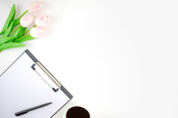 Top view image on a white table with tulips, clipboard, pens and coffee on a white background.