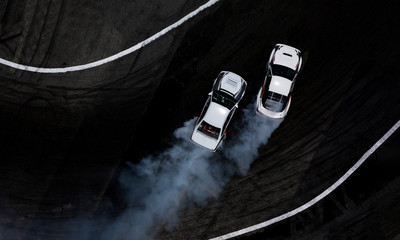 Aerial top view two cars drifting battle on asphalt race track with lots of smoke from burning...