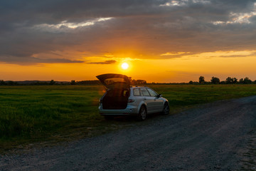 Fototapeta na wymiar A car parked on a field at sunset in a rural landscape