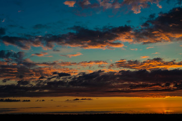 Evening sky at sunset background. Dark clouds hanging above horizon. Majestic cloudscape in blue, orange, violet shades. Grey cloudlets bringing rain. Countryside skyline in twilight time